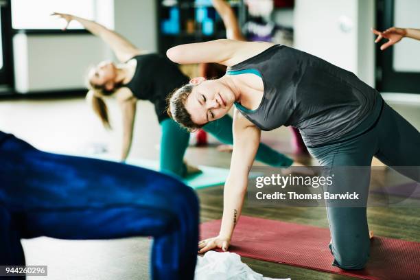 Sweating woman with one arm in half circle pose during hot yoga class in exercise studio