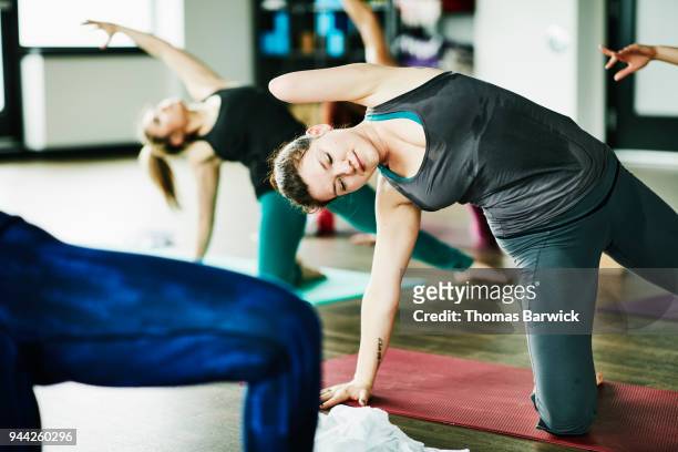 Sweating woman with one arm in half circle pose during hot yoga class in exercise studio