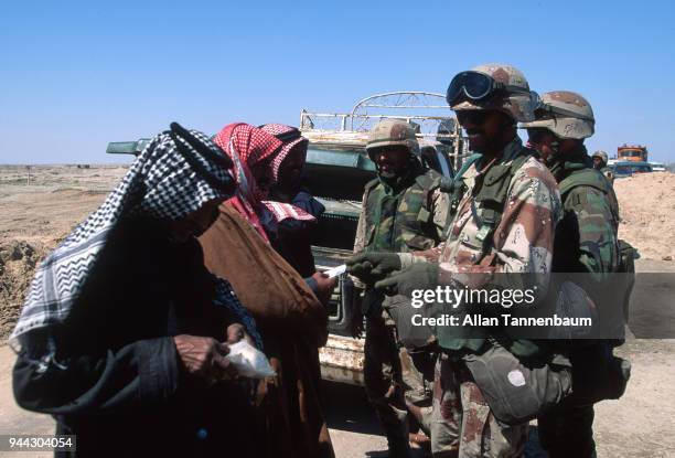 During the Gulf War, American soldiers smile as they examine the documents of a trio of men at a checkpoint, Iraq, 1991.