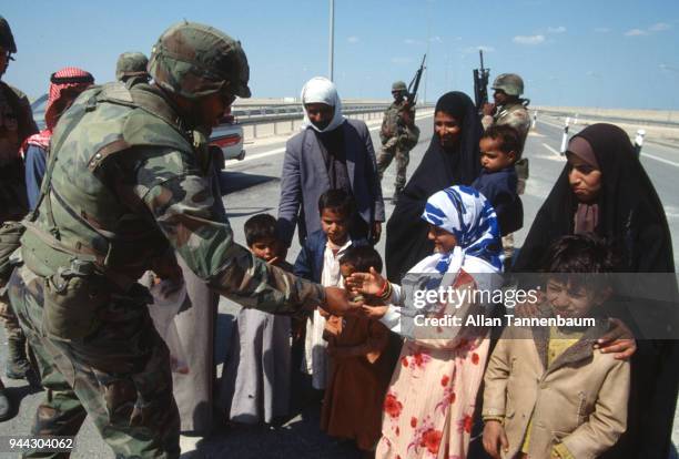 At a checkpoint, American soldiers give candy to a group of children during the Gulf War, Iraq, 1991.