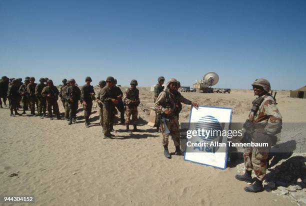 During the Gulf War, a group of American soldiers as they stand in line next to an AT&T sign, Iraq, 1991. The American telecommunications company...