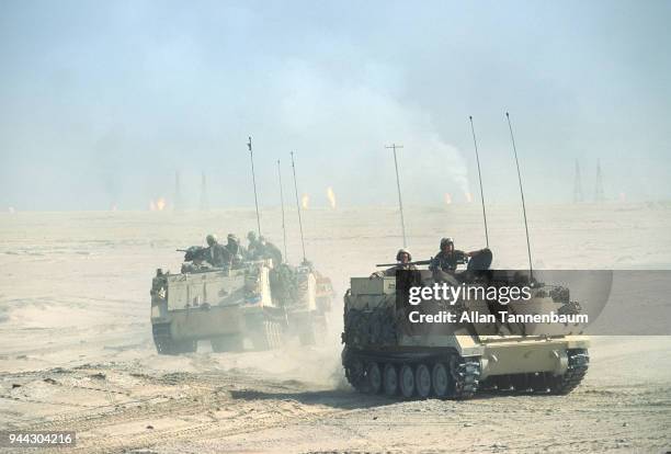 View of American M113 Armored Personnel Carriers as they cross the desert during the Gulf War, Iraq Burning oil wells are visible in the background.