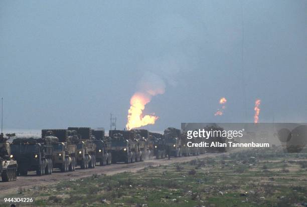During the Gulf War, American military vehicles drive along a road as oil wells burn in the background, Iraq, 1991.