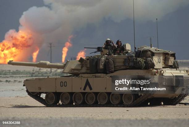 During the Gulf War, a pair of American soldiers stand in the turret of an M1A1 Abrams tank as, near the border with Iraq, oil wells burn in the...