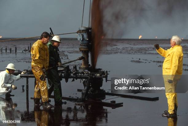 During the Gulf War, oil workers work to cap a well in a blowout, Kuwait, 1991. Other wells burn in the background.