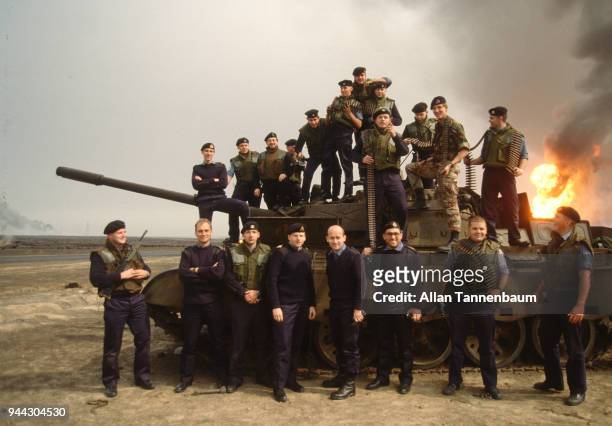 Group portrait of a British soldiers during the Gulf War as they pose around a tank while an oil wells burns in the background, Kuwait, 1991.