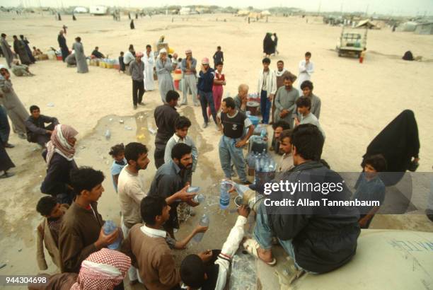 Elevated view of refugees as they fill plastic bottles with water from a hose during the Gulf War, Iraq, 1991. Others wait to fill other containers.