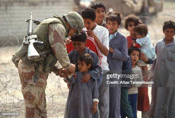 During the Gulf War, an American soldier writes something on the hand of a young boy at the head od a line of children, Iraq, 1991.