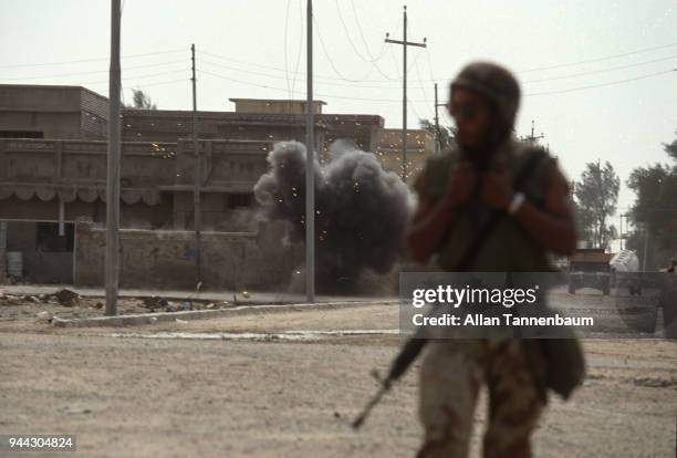 View of sparks and smoke from an unspecified detonation during the Gulf War, as an American soldier walks in the foreground, Kuwait, 1991.