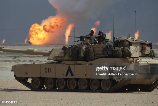 During the Gulf War, a pair of American soldiers stand in the turret of an M1A1 Abrams tank as, near the border with Iraq, oil wells burn in the...