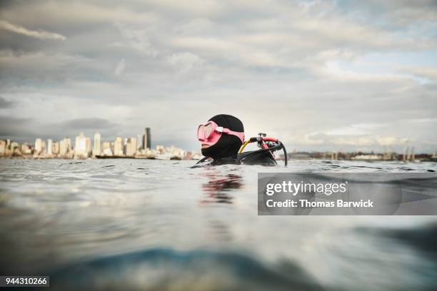 smiling female diver at surface of water before open water dive with cityscape in background - dive adventure foto e immagini stock