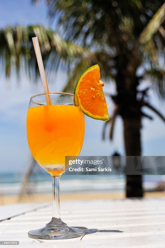 Glass of Orange cocktail by palm tree on beach