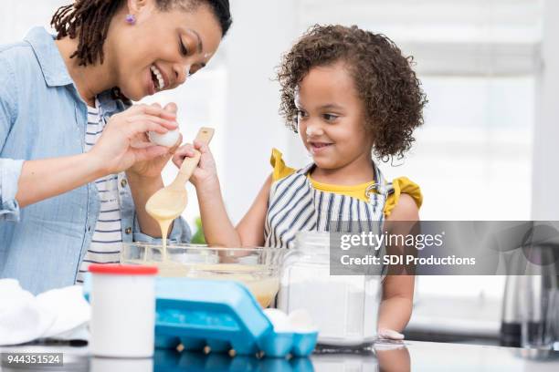 little girl learns how to cracks eggs while baking with mom - crack spoon stock pictures, royalty-free photos & images
