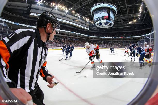 Referee Kelly Sutherland watches as Garnet Hathaway of the Calgary Flames plays the puck while Jacob Trouba of the Winnipeg Jets defends during first...