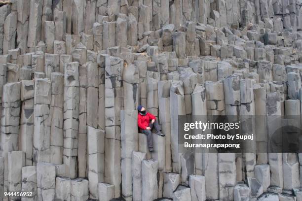 reynisfjall mountain cliff basalt column at reynisfjara black sand beach in south coast,iceland.a man in red jacket sitting on basalt column cliff  looking at beautiful landscape inspiration and motivation concept. - basalt stockfoto's en -beelden