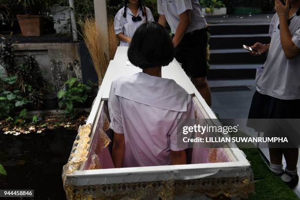 This photo taken on March 30 shows a Thai teenager trying out a traditional coffin at the Kid Mai Death Awareness Cafe, an exhibition space built to...