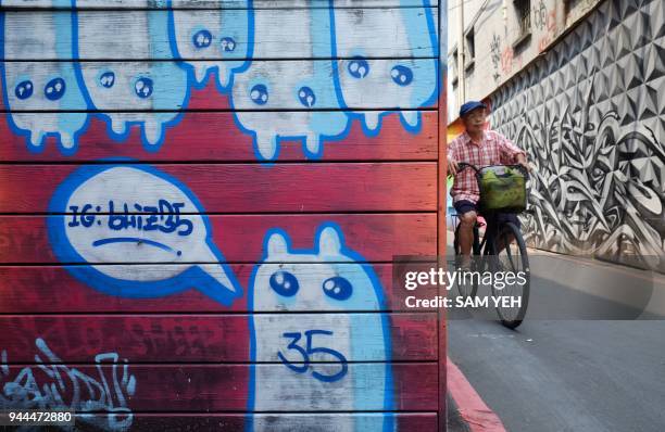 This picture taken on April 10, 2018 shows a man riding past street art murals in Taipei's Ximen district. / AFP PHOTO / SAM YEH