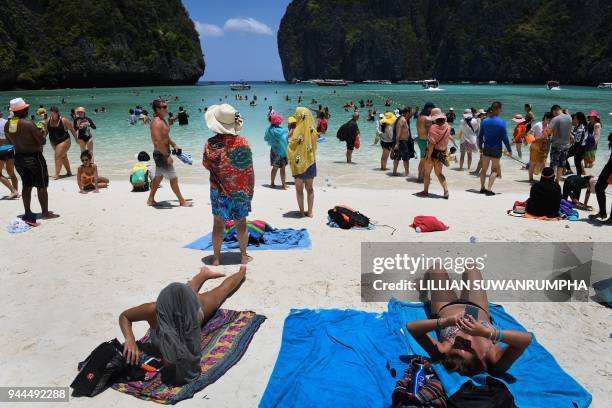 This photo taken on April 9, 2018 shows tourists sunbathing and walking on Maya Bay, on the southern Thai island of Koh Phi Phi. Across the region,...