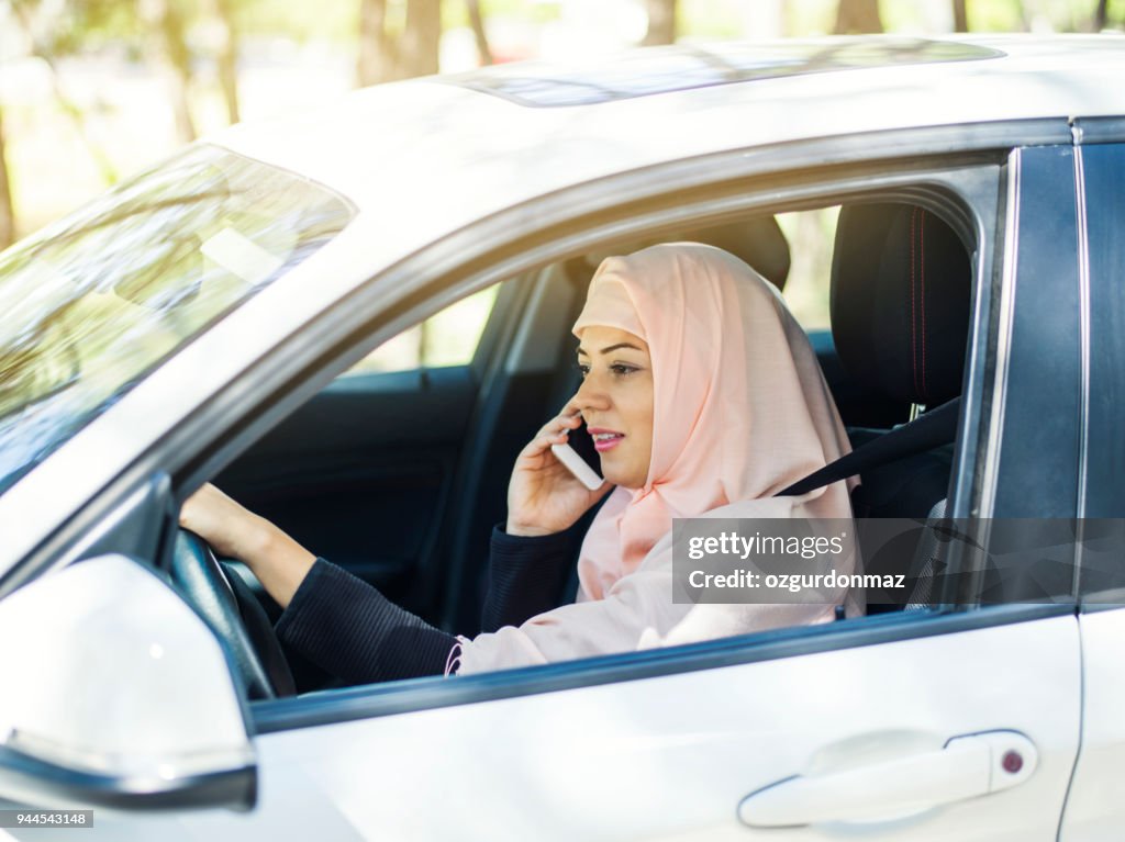 Muslimische Frau mit Smartphone während der Fahrt Auto