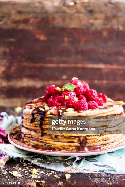 stack of wheat golden pancakes or pancake cake with freshly picked raspberry, chopped pistachios, chocolate sauce on a dessert plate, selective focus - raspberry sauce stock pictures, royalty-free photos & images