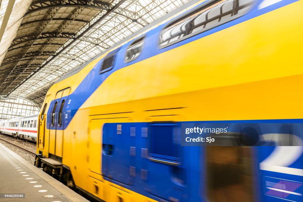 Treinen op het spoorlijnen in Amsterdam Centraalstation. Een IC-dubbledecker van de Nederlandse spoorwegen (NS) vertrekt.