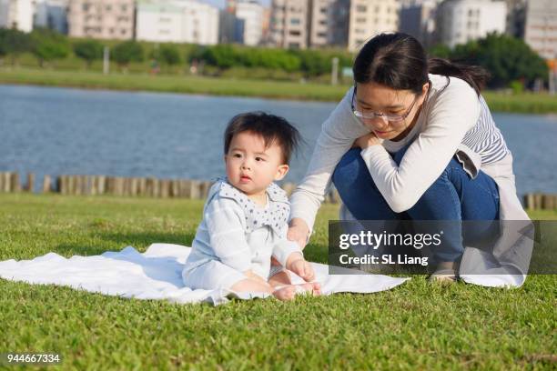 asian mother with her baby at riverside picnic - rivier gras oever stockfoto's en -beelden