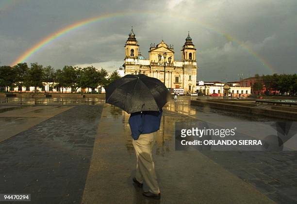 Un hombre camina el 11 de junio de 2003 por la Plaza de la Constitución en la ciudad de Guatemala, mientras observa el arcoiris que se forma sobre la...