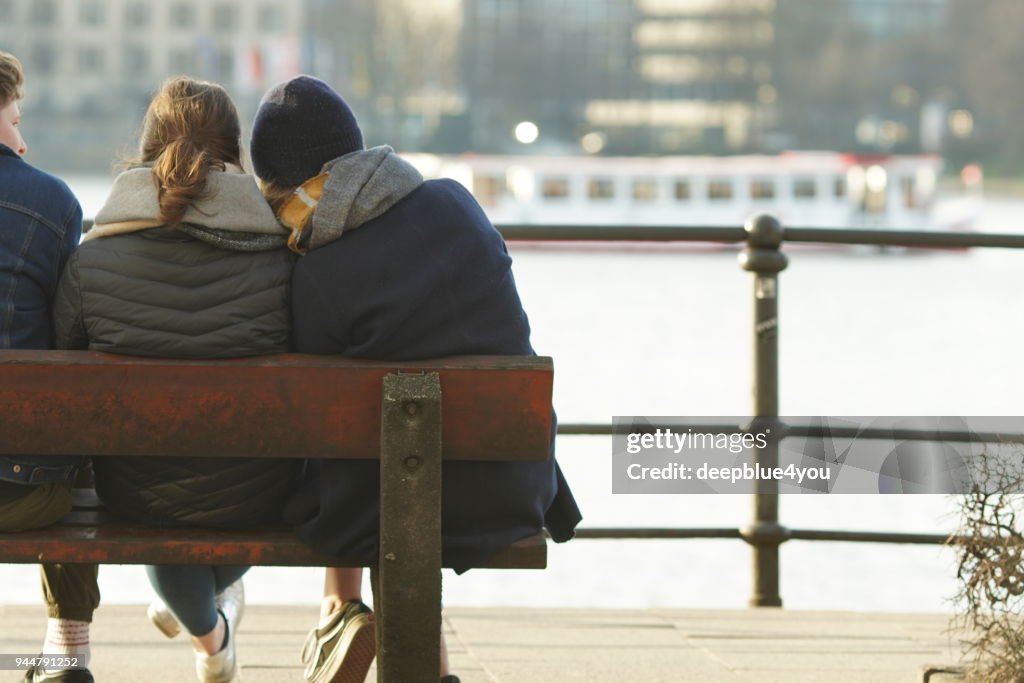 Young people sitting on a bench in the sunshine and looking at the Hamburger Alster lake