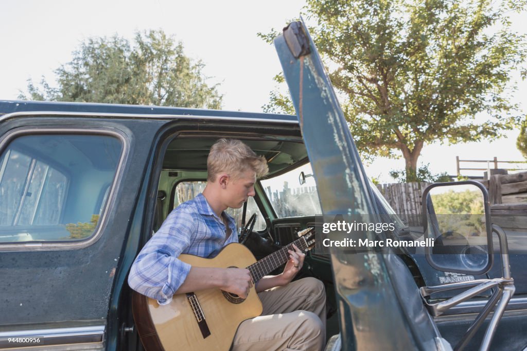 Teen boy playing guitar in pick up truck