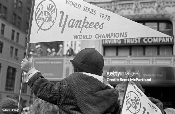 New York - A young boy sits on his fathers shoulders and holds a Yankees banner at a ticker tape parade celebrating their World Series win.