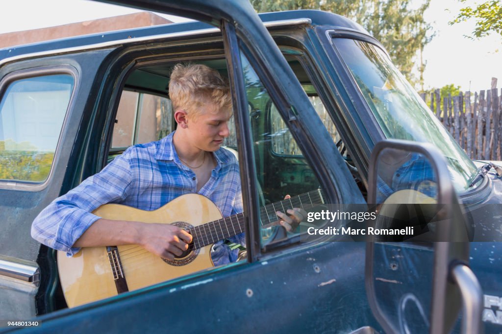 Teen boy playing guitar in pick up truck