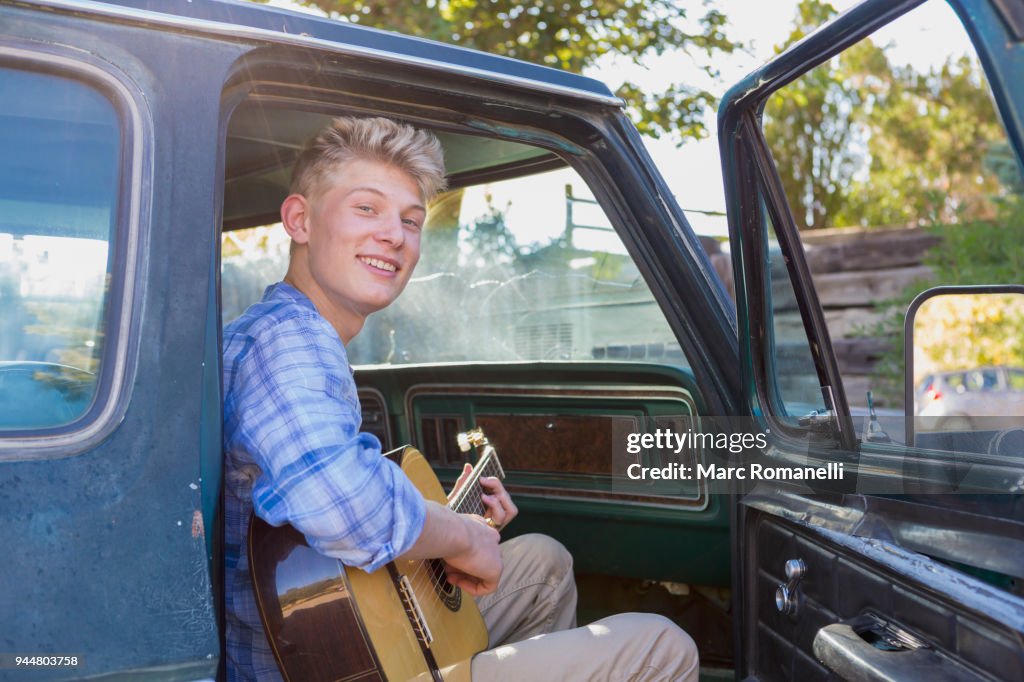 Teen boy playing guitar in pick up truck