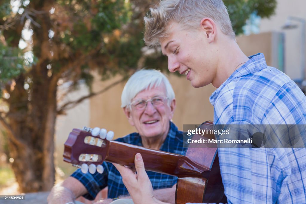 Teen boy playing guitar with with grandfather listening