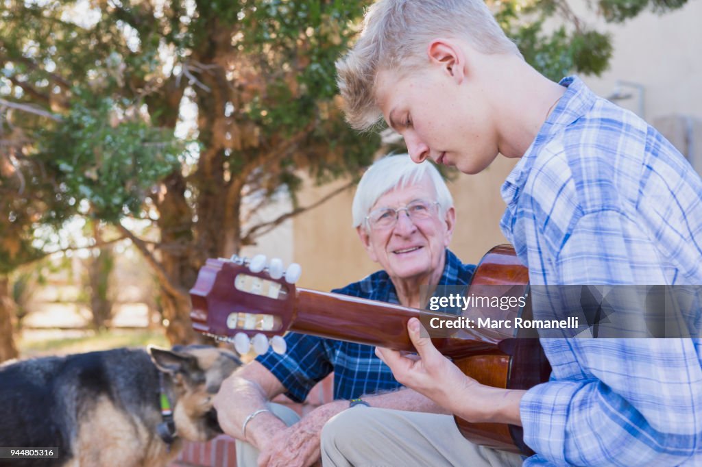Teen boy playing guitar with with grandfather listening