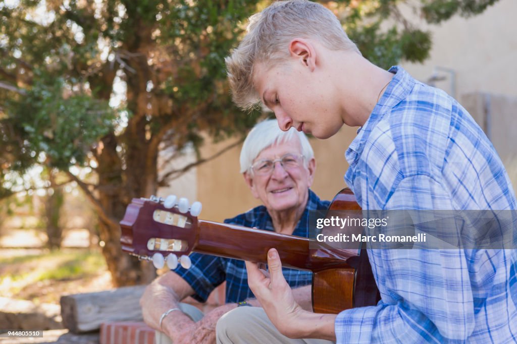 Teen boy playing guitar with with grandfather listening