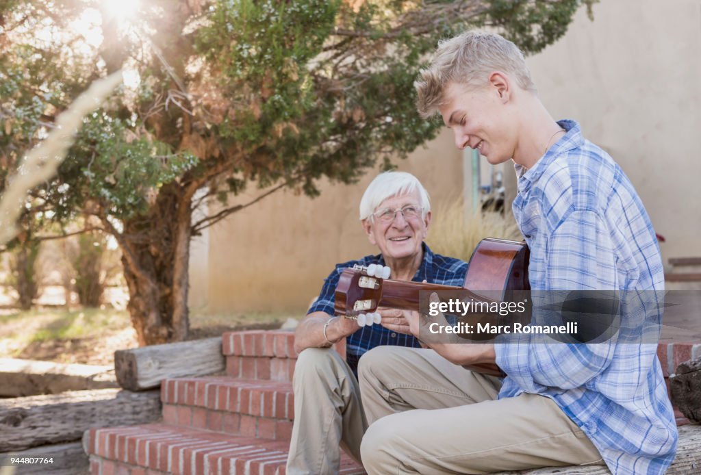 Teen boy playing guitar with with grandfather listening