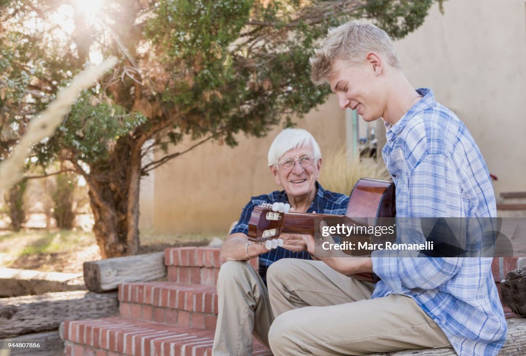 Teen boy playing guitar with with grandfather listening