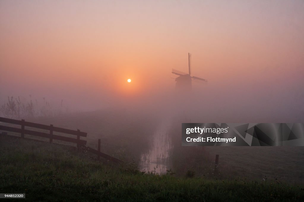 Misty morning sunrise with silhouette of a windmill