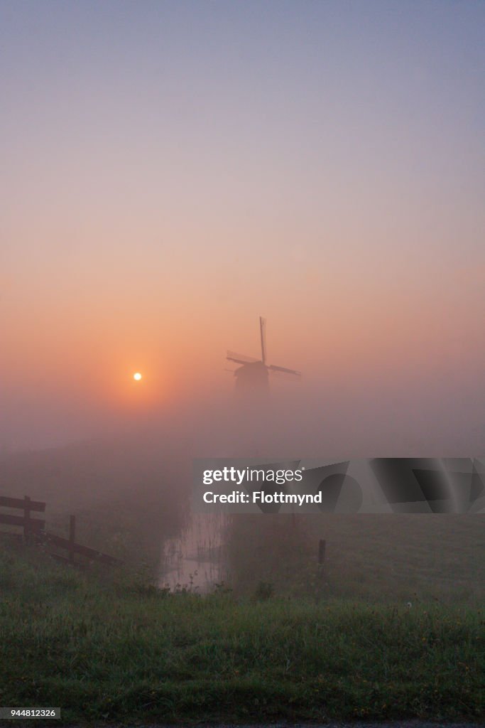 Misty morning sunrise with silhouette of a windmill