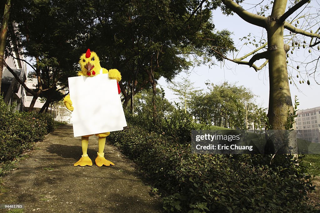 Person in chicken costume wearing signboard in forest