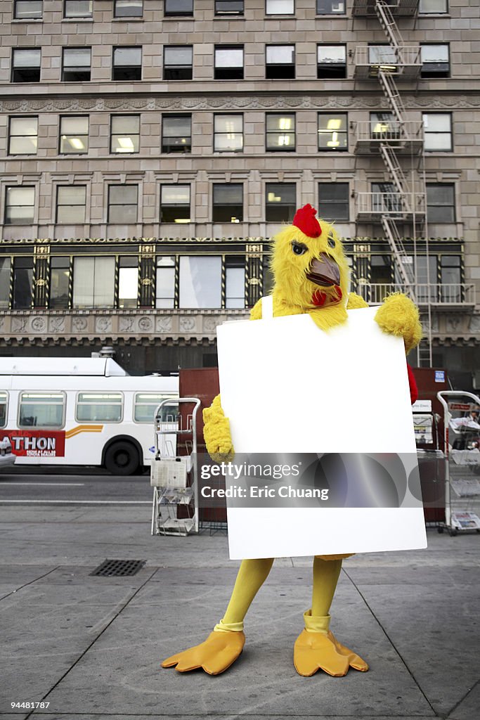 Person in chicken costume wearing signboard