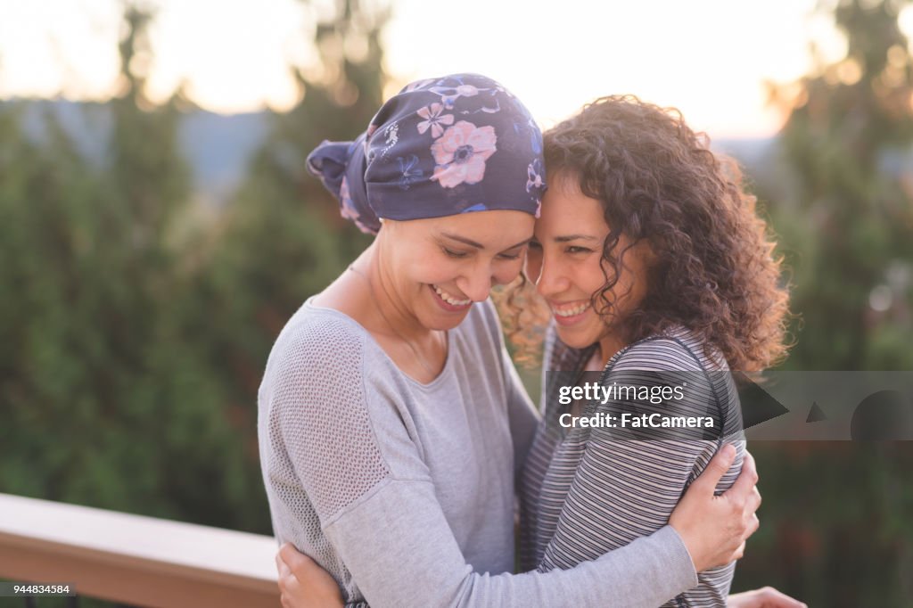 Hermosa mujer étnica, luchando contra el cáncer abraza a su hermana bien