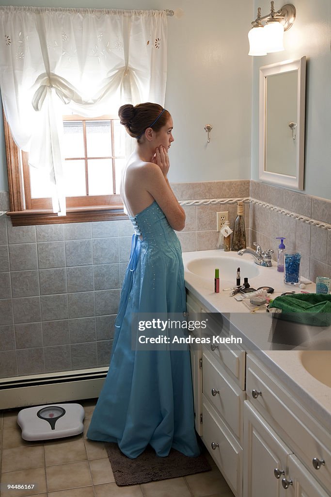 Teenage girl in prom dress looking in mirror.