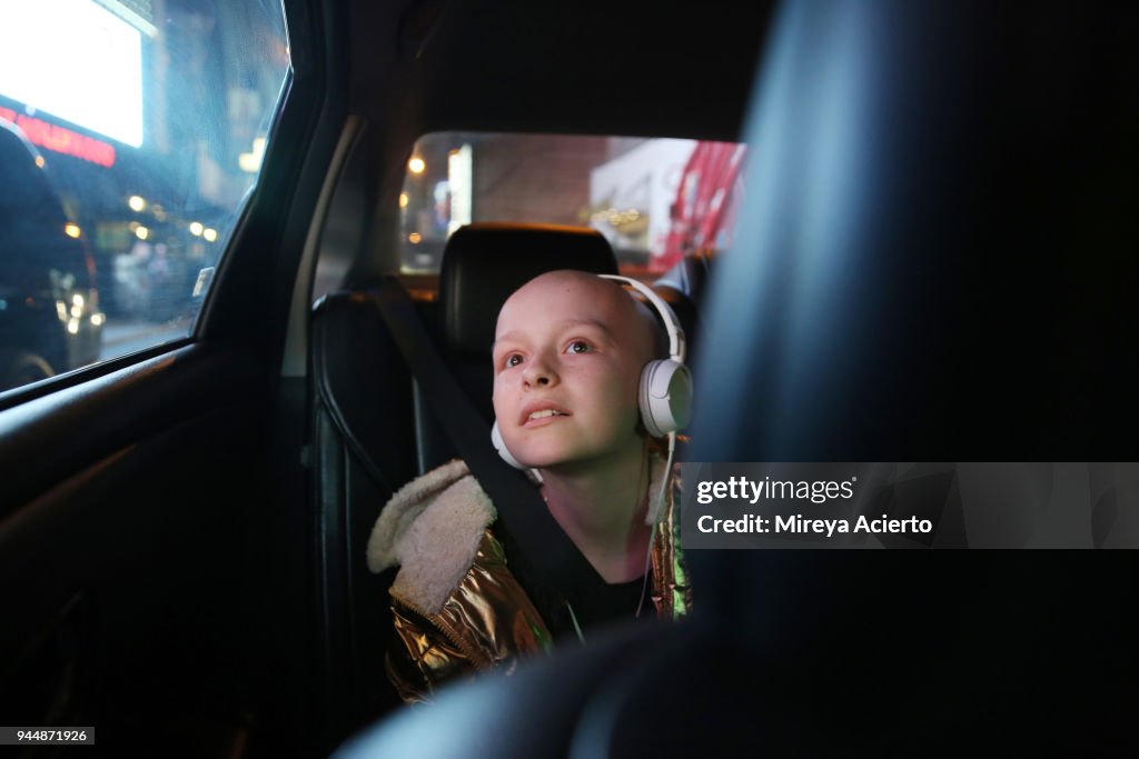 A young girl with cancer, riding in a car, looks at all the bright lights of the city.