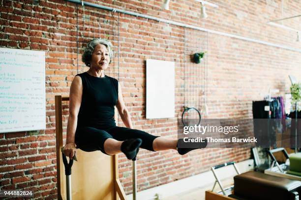 mature woman doing arm press on high-low pilates chair in fitness studio - best animated short film stock-fotos und bilder