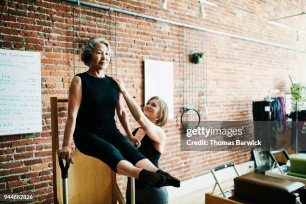 female pilates instructor assisting mature student on high-low chair during class in exercise studio - fitness instructor stock-fotos und bilder