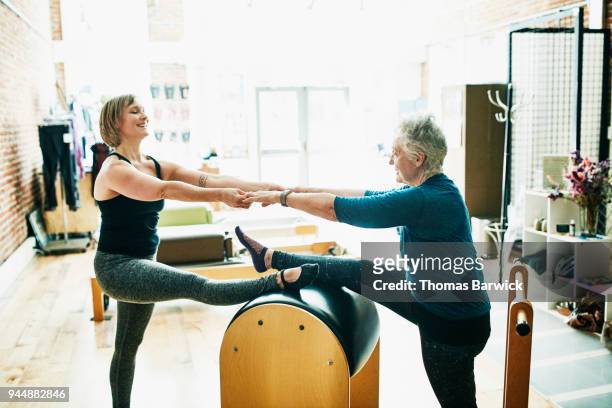 Mature mother and daughter practicing pilates ladder barrel partner stretch together in fitness studio