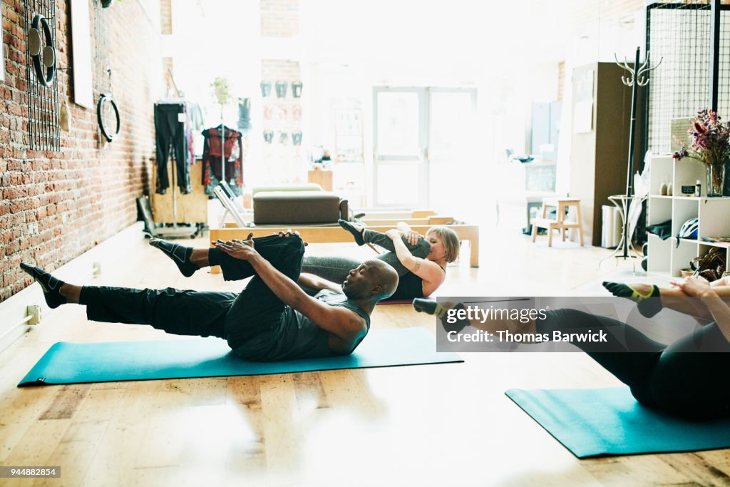 Mature male pilates student practicing single leg mat stretch during class in pilates studio