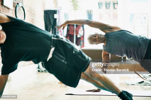 two mature men performing side plank on mat during pilates class in exercise studio - side plank pose stock pictures, royalty-free photos & images