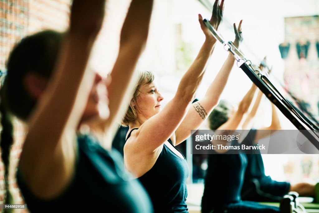 Woman using reformer arm straps during pilates class in fitness studio